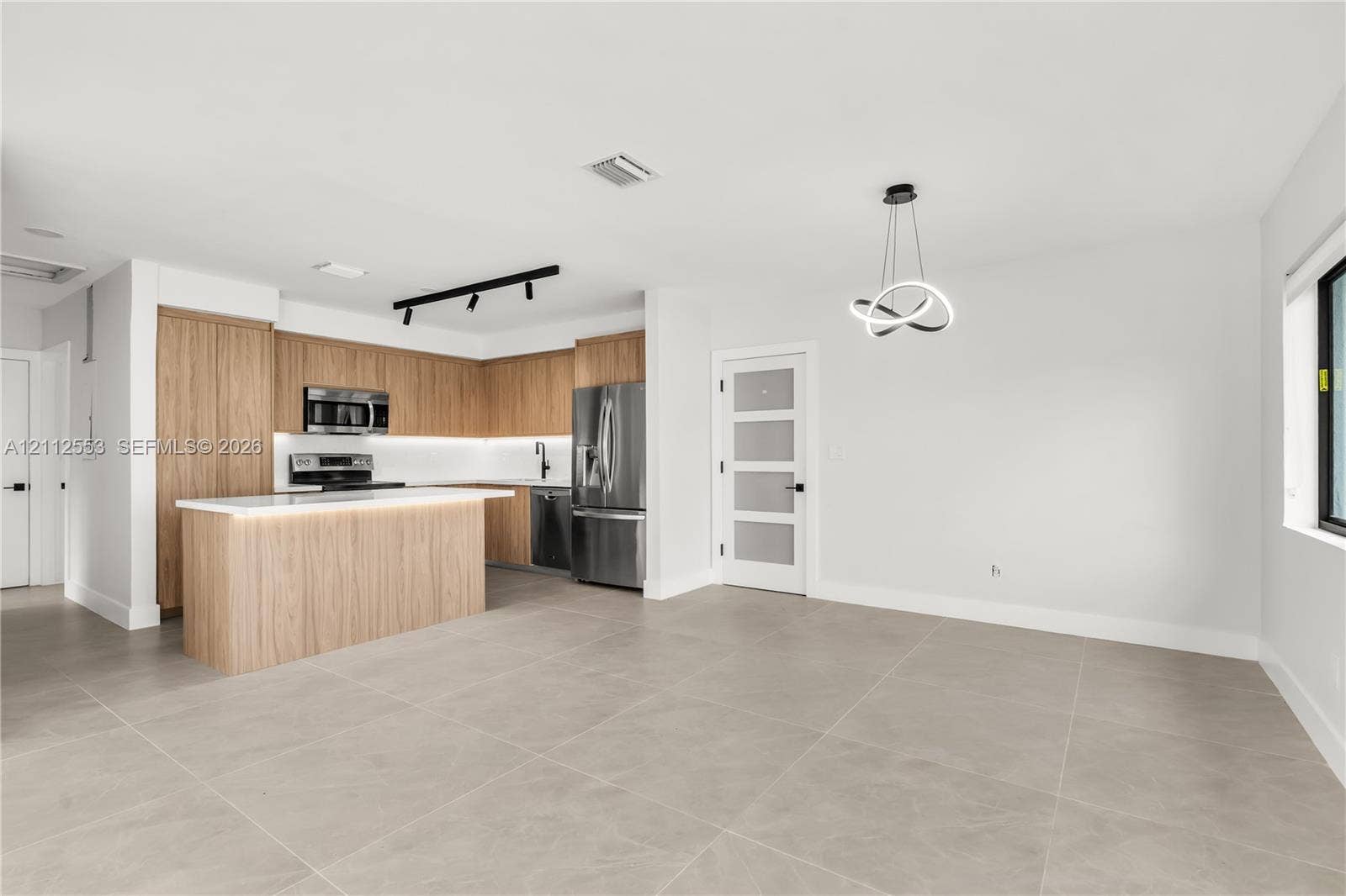 Kitchen featuring wood-finish cabinetry, a central island with a quartz countertop, stainless steel appliances, matte black track lighting, and large-format tile flooring