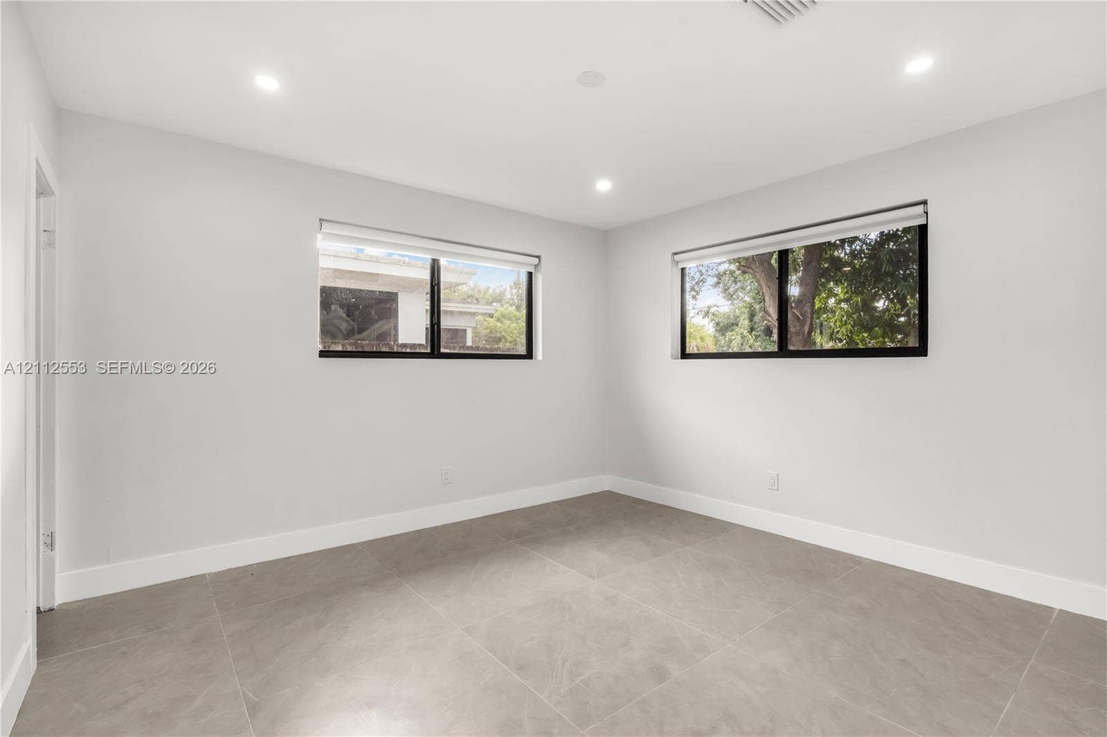 Neutral-toned room featuring large-format tile flooring, dual windows with black frames, recessed ceiling lighting, and smooth-finish walls