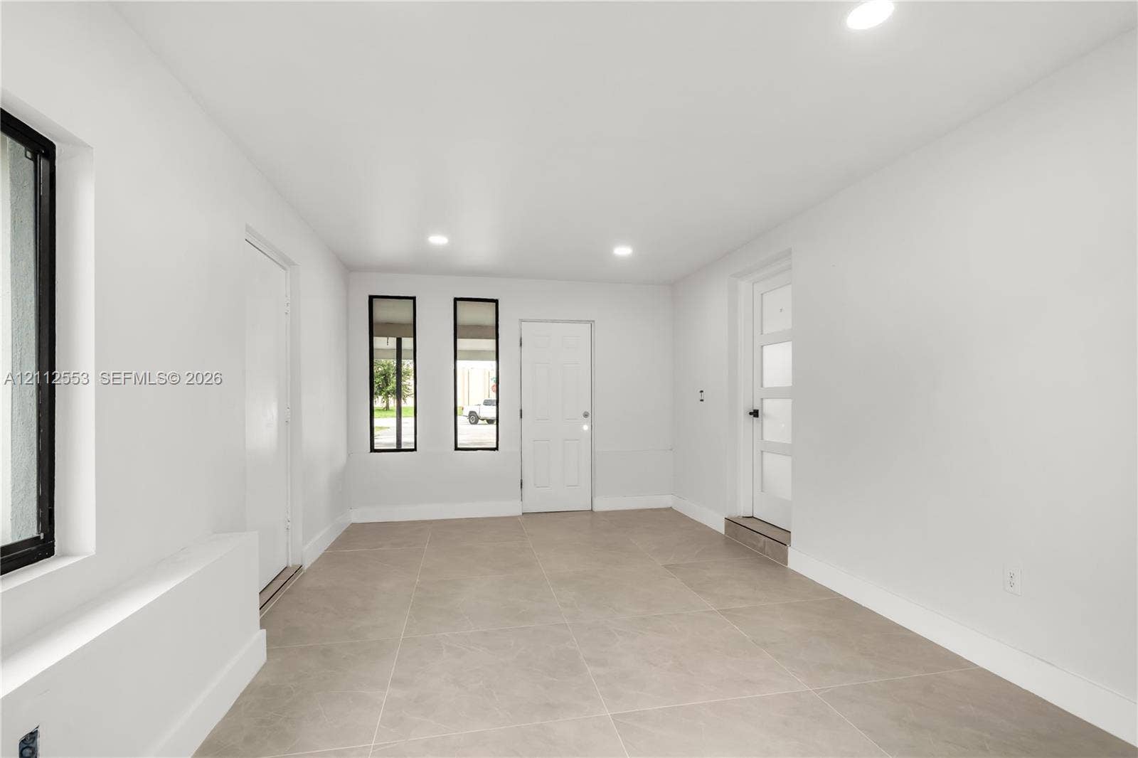 Neutral-toned large-format tile flooring, recessed ceiling lighting, multi-pane glass entry door, and vertical windows with black frames