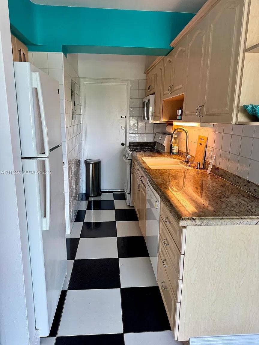 8400 Byron Avenue, #4E, Miami Beach, Miami Beach, FL 33141 Galley kitchen featuring stone countertops, white tile backsplash, light wood-tone cabinetry, and checkered tile flooring