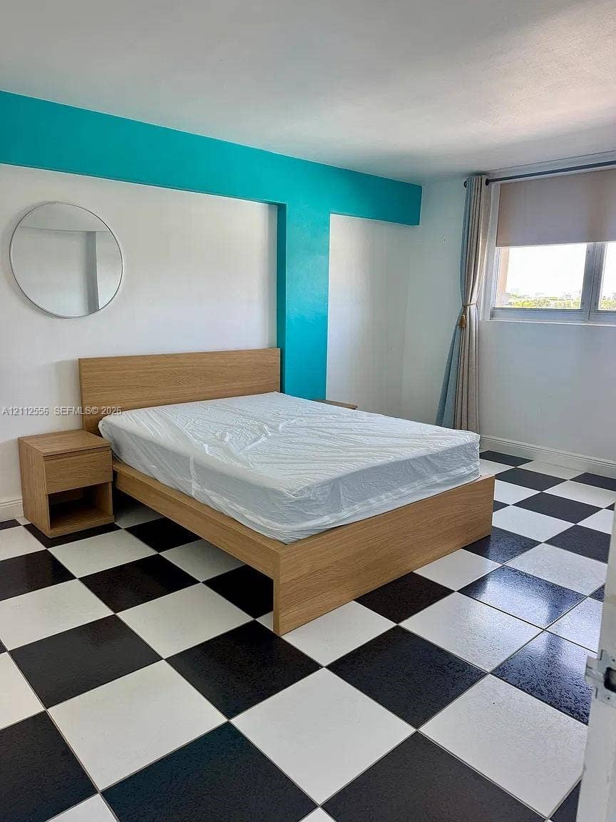 8400 Byron Avenue, #4E, Miami Beach, Miami Beach, FL 33141 Room featuring black and white checkerboard tile flooring, a circular wall-mounted mirror, and an accent wall painted in a vibrant teal tone