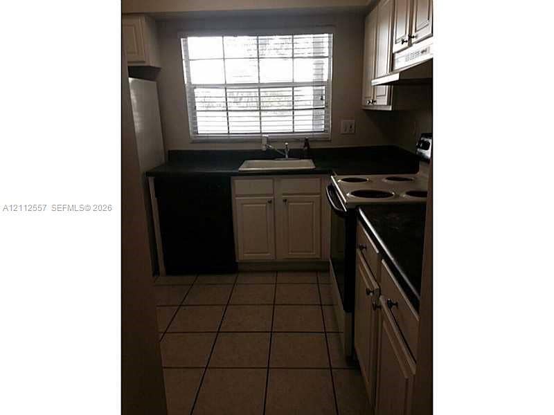 2121 NW 96th Terrace, #14J, Pembroke Pines, Pembroke Pines, FL 33024 Kitchen featuring light-toned cabinetry, dark solid-surface countertops, tile flooring, and a window above a drop-in sink