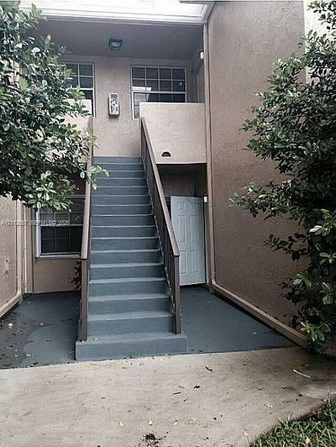 2121 NW 96th Terrace, #14J, Pembroke Pines, Pembroke Pines, FL 33024 Stucco exterior featuring an enclosed staircase with painted concrete treads and metal handrails, leading to a recessed entry with a paneled door and multi-light windows