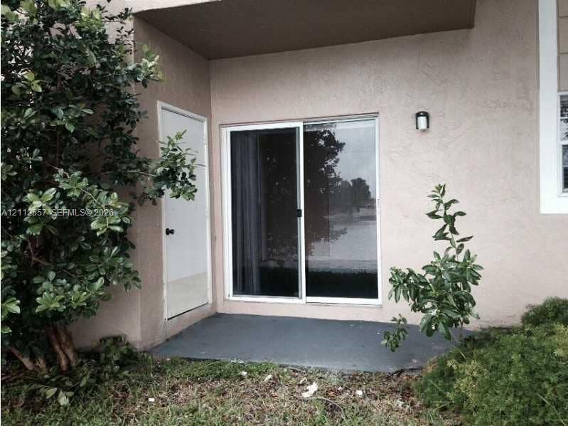 2121 NW 96th Terrace, #14J, Pembroke Pines, Pembroke Pines, FL 33024 Exterior patio area featuring a concrete base, sliding glass door, private exterior storage closet, and wall-mounted sconce lighting