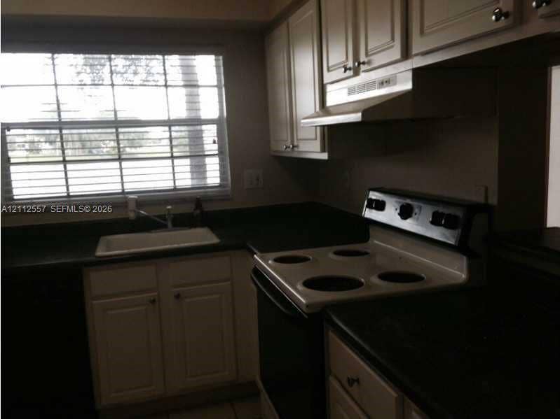 2121 NW 96th Terrace, #14J, Pembroke Pines, Pembroke Pines, FL 33024 Kitchen featuring cabinetry with crown molding, solid-surface countertops, integrated range hood, white drop-in sink, and large multi-pane window