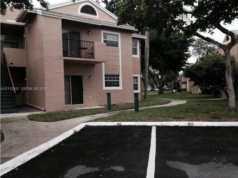 2121 NW 96th Terrace, #14J, Pembroke Pines, Pembroke Pines, FL 33024 Multi-story exterior featuring a stucco facade, arched gable window, upper-level balcony with metal railing, and dedicated asphalt parking spaces