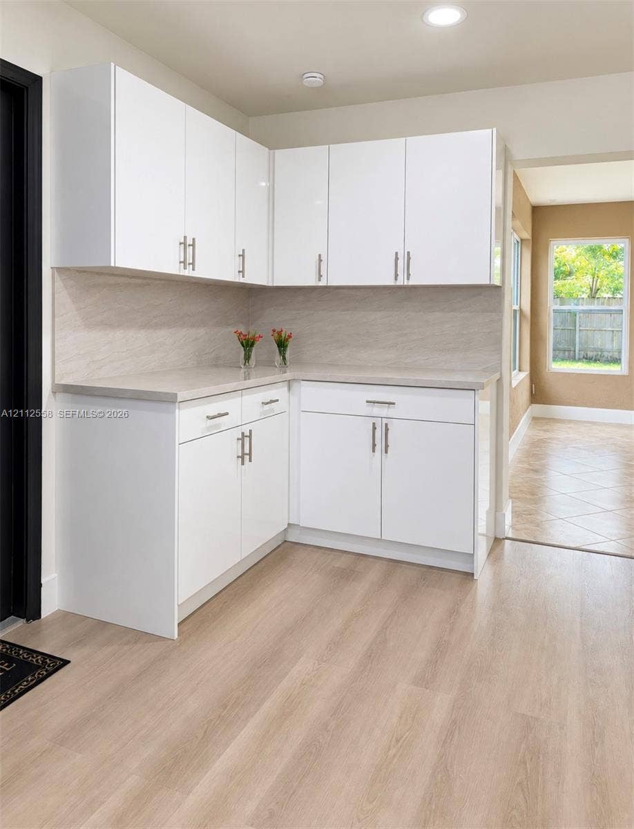 White cabinetry with brushed nickel hardware, stone-finish countertops, full-height stone-patterned backsplash, and wood-finish flooring