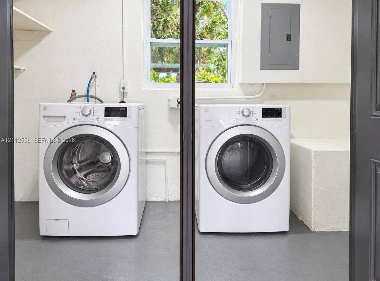 Dedicated utility space featuring built-in shelving, a single-hung window, concrete-finish flooring, and a wall-mounted electrical panel