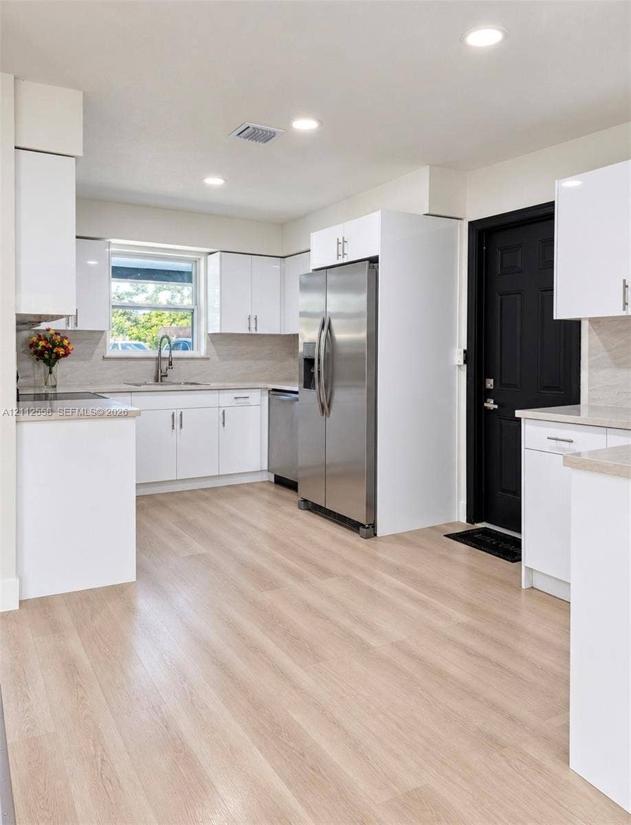 Kitchen featuring high-gloss white cabinetry, light-toned wood-finish flooring, stainless steel appliances, neutral stone-finish countertops, and recessed lighting