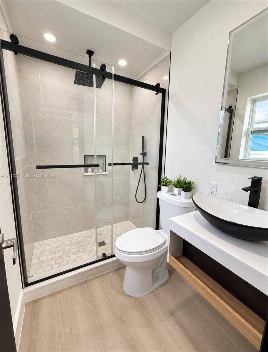 Walk-in shower with sliding black-framed glass door, large-format wall tile, integrated tile niche, and matte black rainfall showerhead