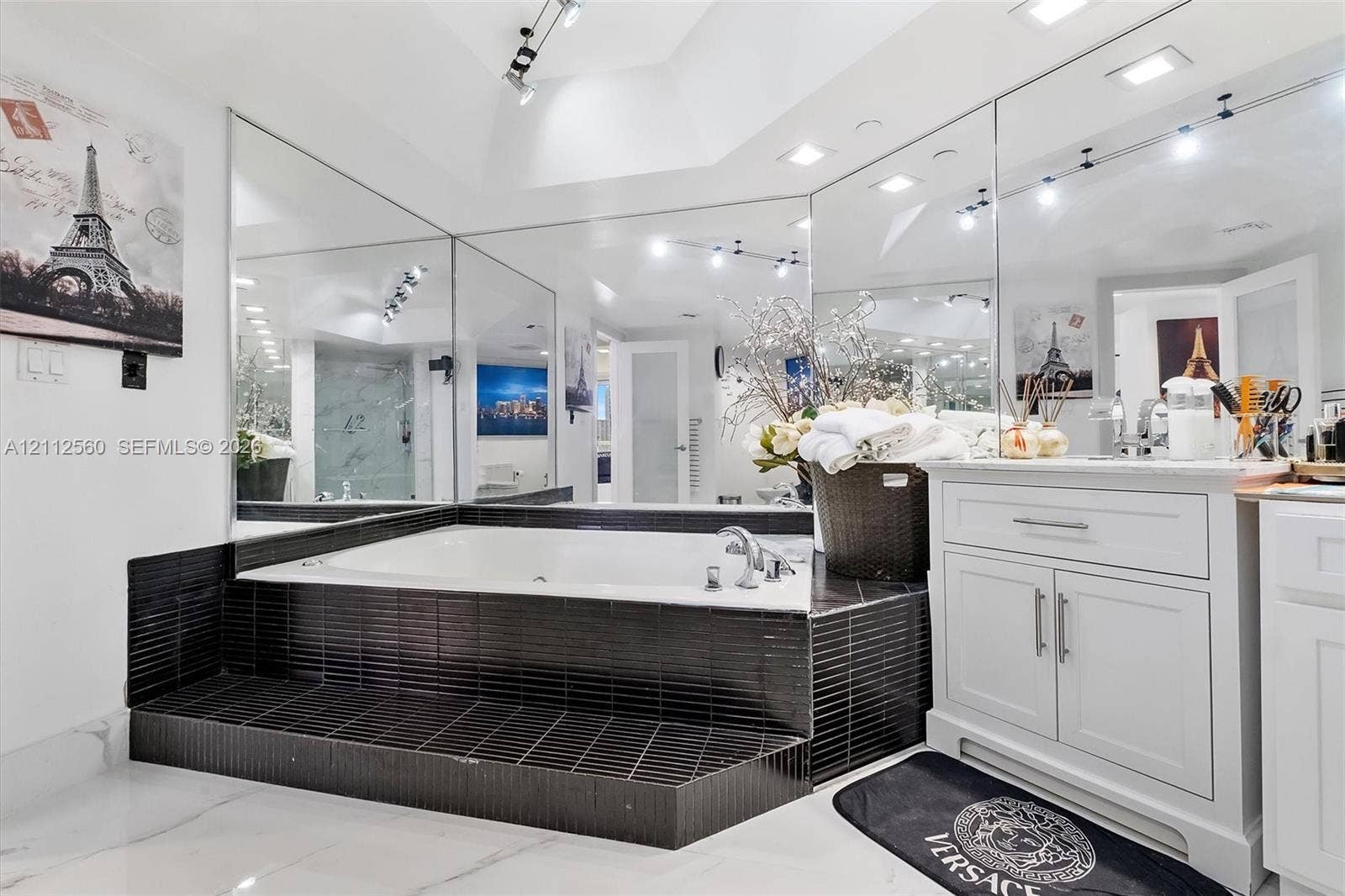 4000 Island Boulevard, #701, Aventura, FL 33160 Sunken jetted tub finished with black linear tile, white cabinetry with silver hardware, full-width wall mirrors, recessed lighting, and large-format flooring