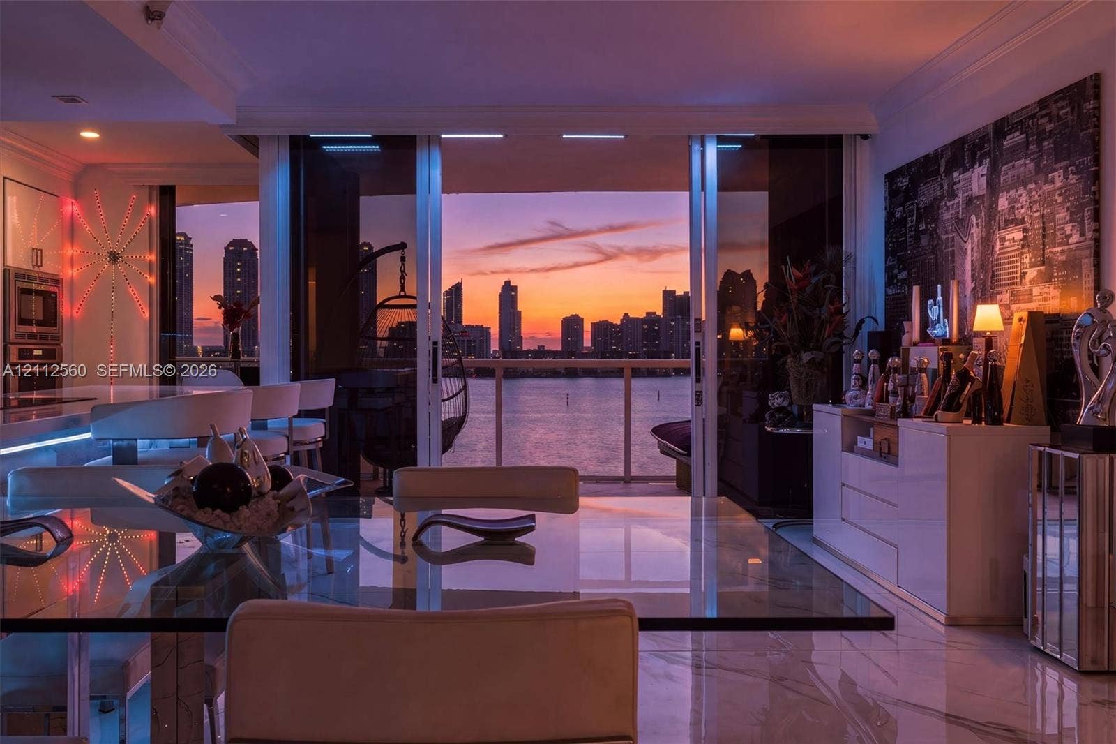 4000 Island Boulevard, #701, Aventura, FL 33160 Floor-to-ceiling sliding glass doors, stone-finish flooring, built-in cabinetry, and integrated kitchen appliances, complemented by a water and cityscape backdrop