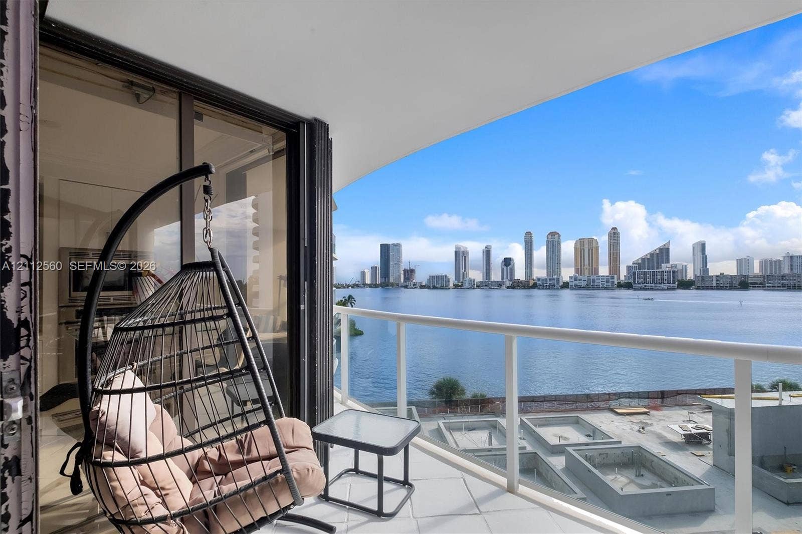 4000 Island Boulevard, #701, Aventura, FL 33160 Covered balcony featuring white railings, tiled flooring, and sliding glass door access, highlighting water and city skyline scenery