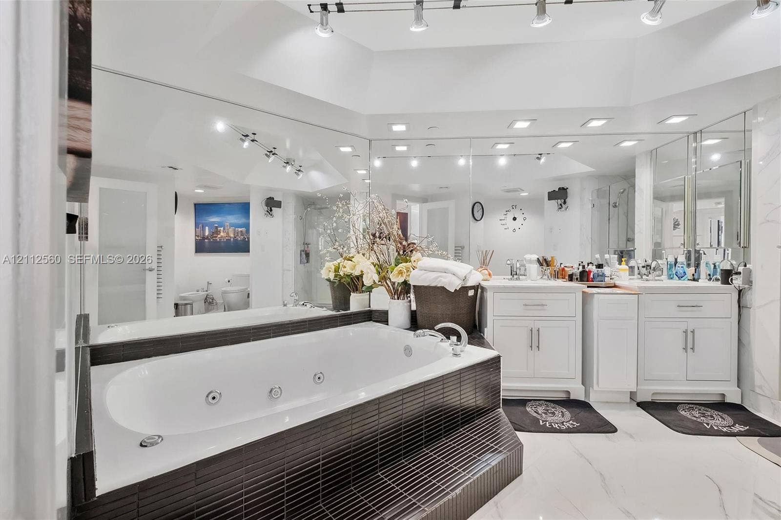 4000 Island Boulevard, #701, Aventura, FL 33160 Jetted soaking tub with black tile surround, double vanity with white cabinetry, expansive wall-to-wall mirrors, recessed lighting, and large-format flooring