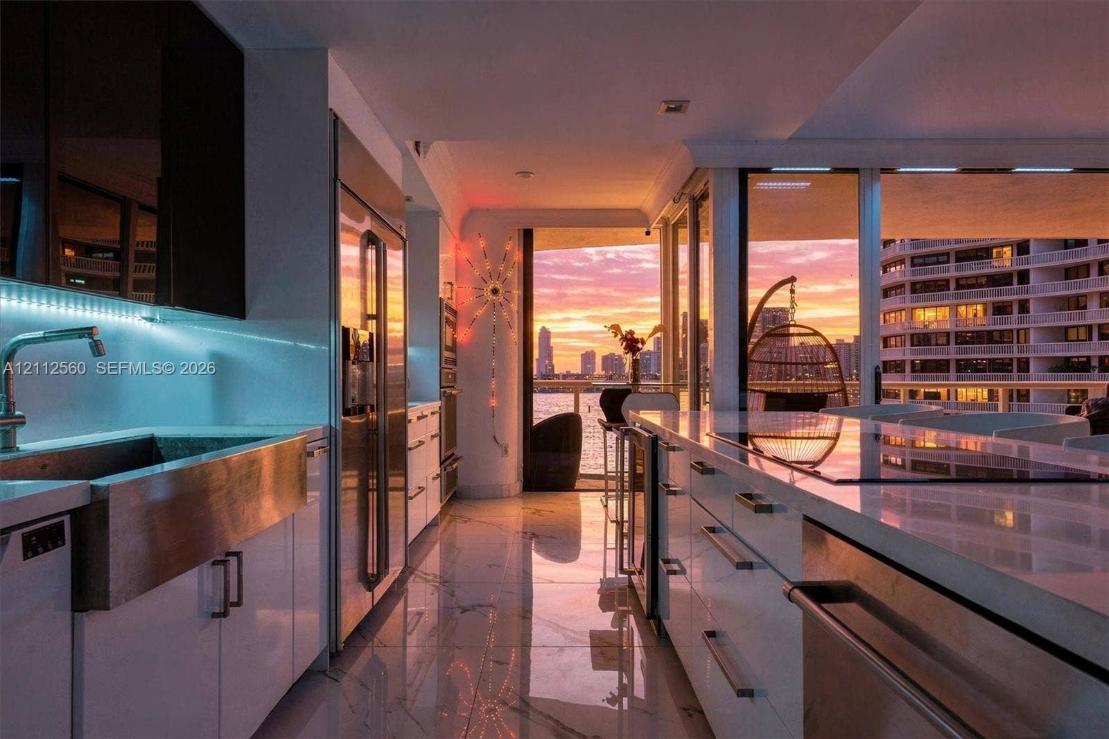 4000 Island Boulevard, #701, Aventura, FL 33160 Modern kitchen featuring sleek white cabinetry, stainless steel apron-front sink, polished stone countertops, integrated stainless steel appliances, and large-format tile flooring