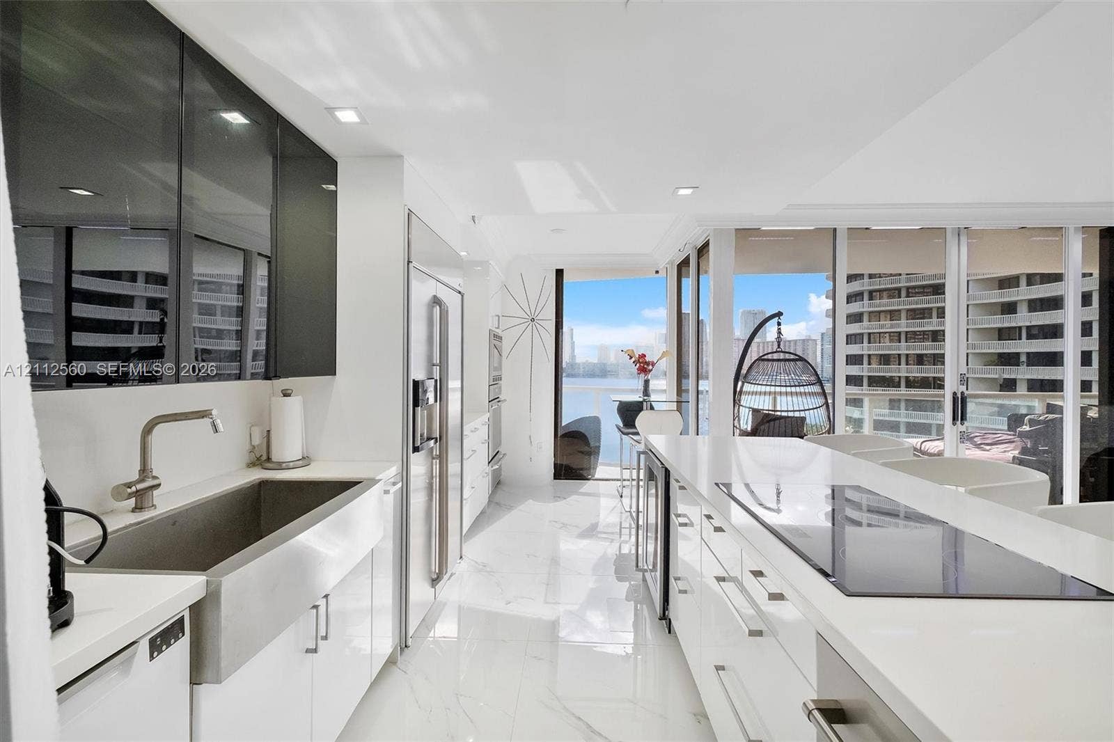 4000 Island Boulevard, #701, Aventura, FL 33160 Kitchen featuring high-gloss cabinetry, stainless steel farmhouse sink, white stone-surfaced countertops, built-in appliances, and floor-to-ceiling windows
