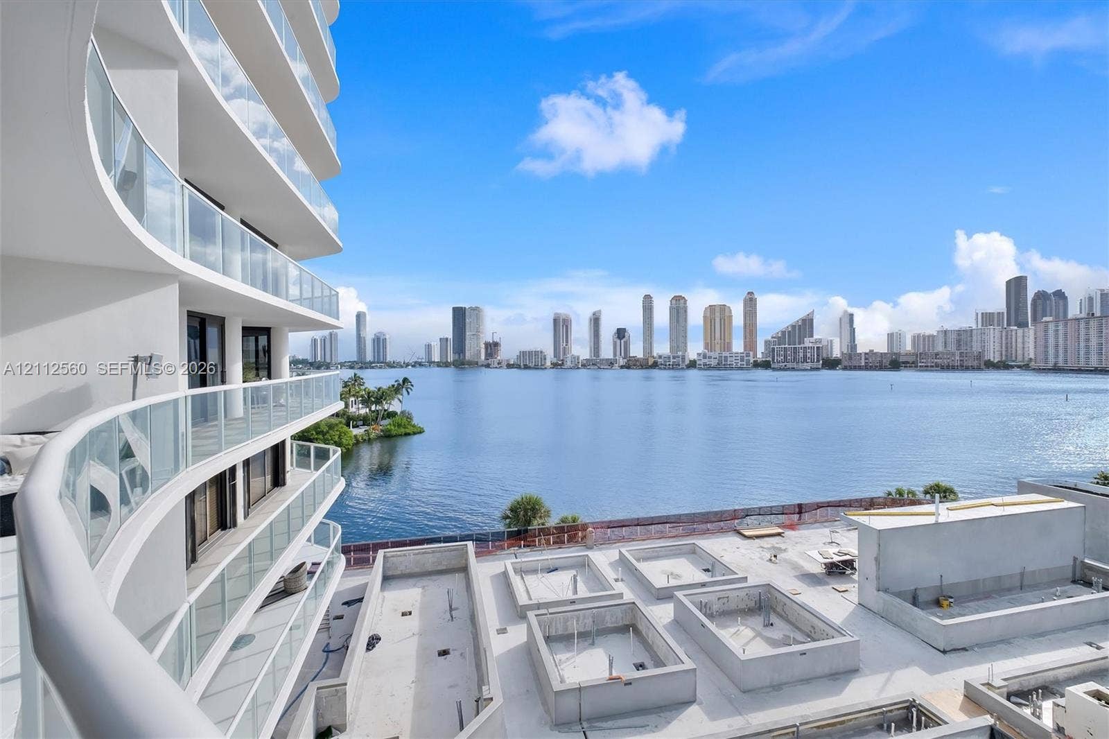 4000 Island Boulevard, #701, Aventura, FL 33160 Curved exterior balconies with glass railings overlooking a large body of water and an urban skyline
