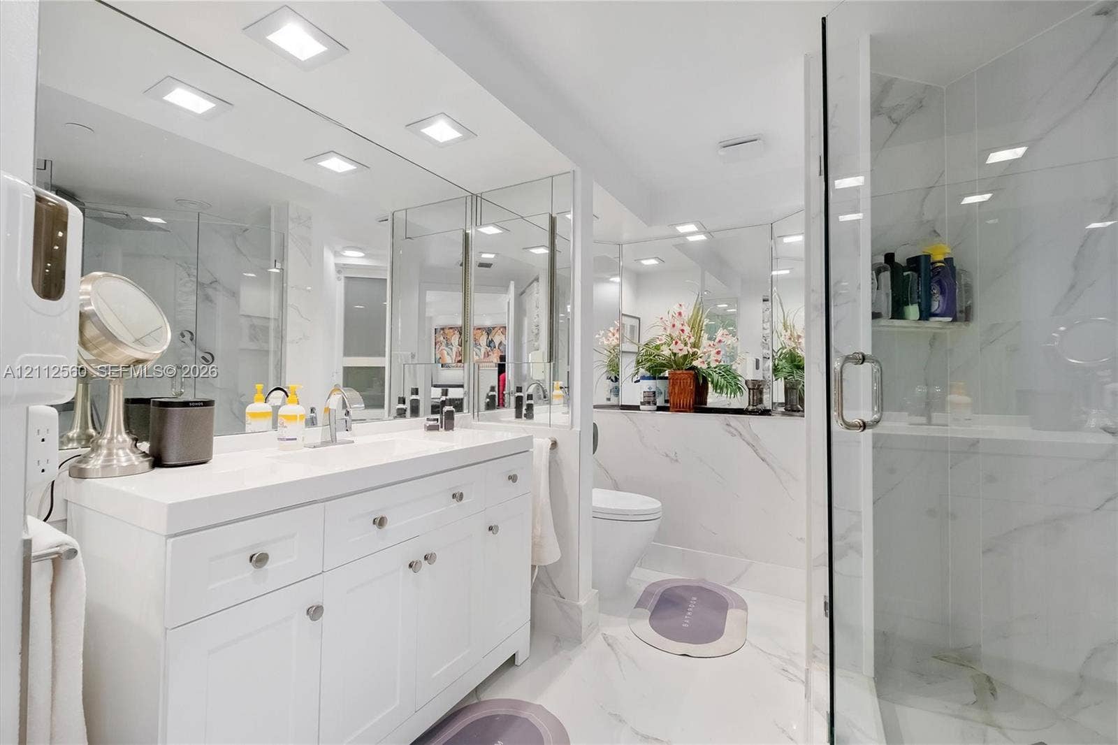 4000 Island Boulevard, #701, Aventura, FL 33160 White vanity with an integrated countertop, full-width wall mirror, recessed ceiling lighting, and a glass-enclosed shower featuring large-format veined tile finishes