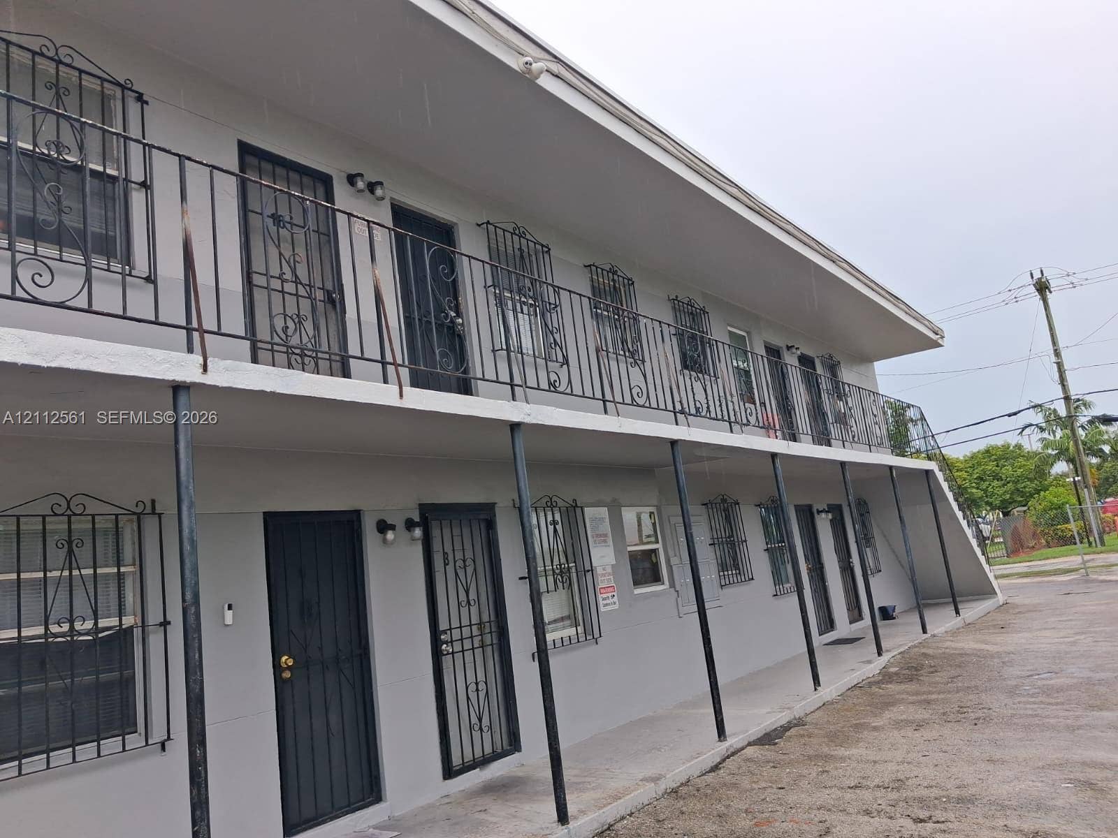 6901 NW 8th Avenue, #2, Miami, Miami, FL 33150 Two-story exterior featuring a neutral painted facade, metal security bars on windows and doors, covered concrete walkways, and an integrated staircase
