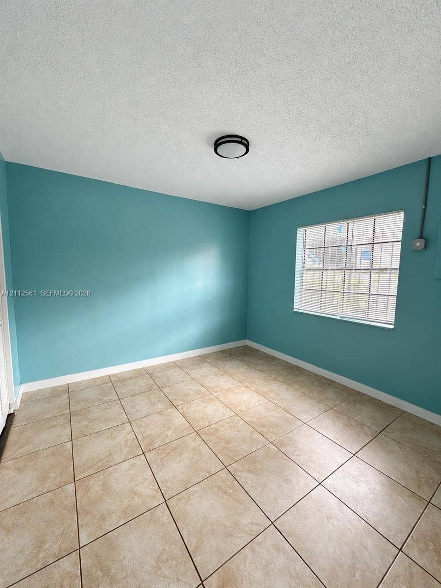 6901 NW 8th Avenue, #2, Miami, Miami, FL 33150 Interior room featuring large-format ceramic tile flooring, a multi-pane window with blinds, and a flush-mount circular ceiling light fixture