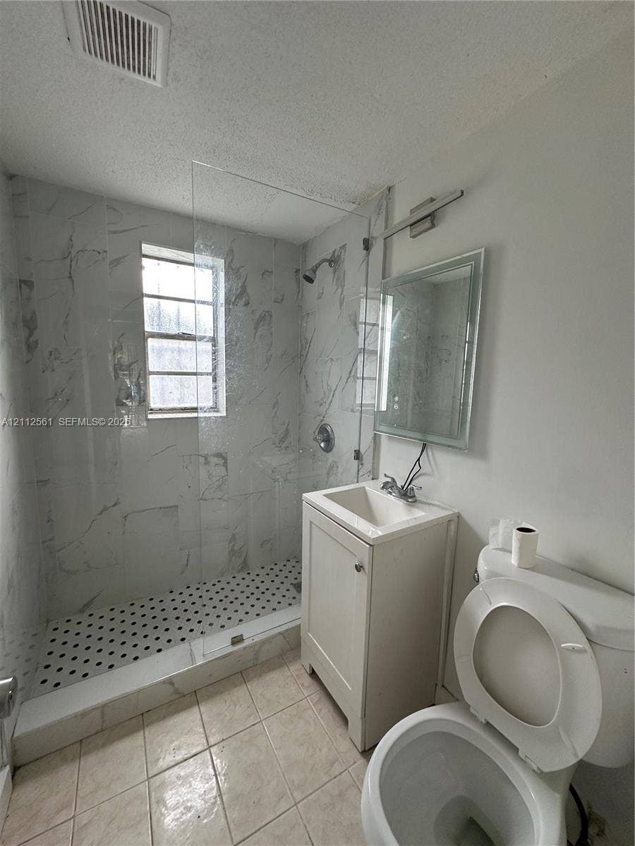 6901 NW 8th Avenue, #2, Miami, Miami, FL 33150 Walk-in shower with floor-to-ceiling stone-finish tile surround and glass partition, basketweave-pattern tile shower floor, and a single-basin vanity cabinet