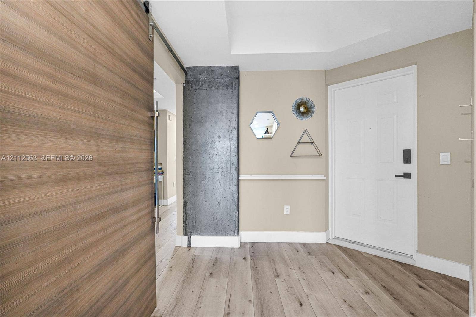 3330 NE 190th Street, #2016, Aventura, FL 33180 Entryway featuring wood-finish flooring, a sliding wood-finish barn door, an exposed concrete pillar, and a white panel door with integrated electronic lock
