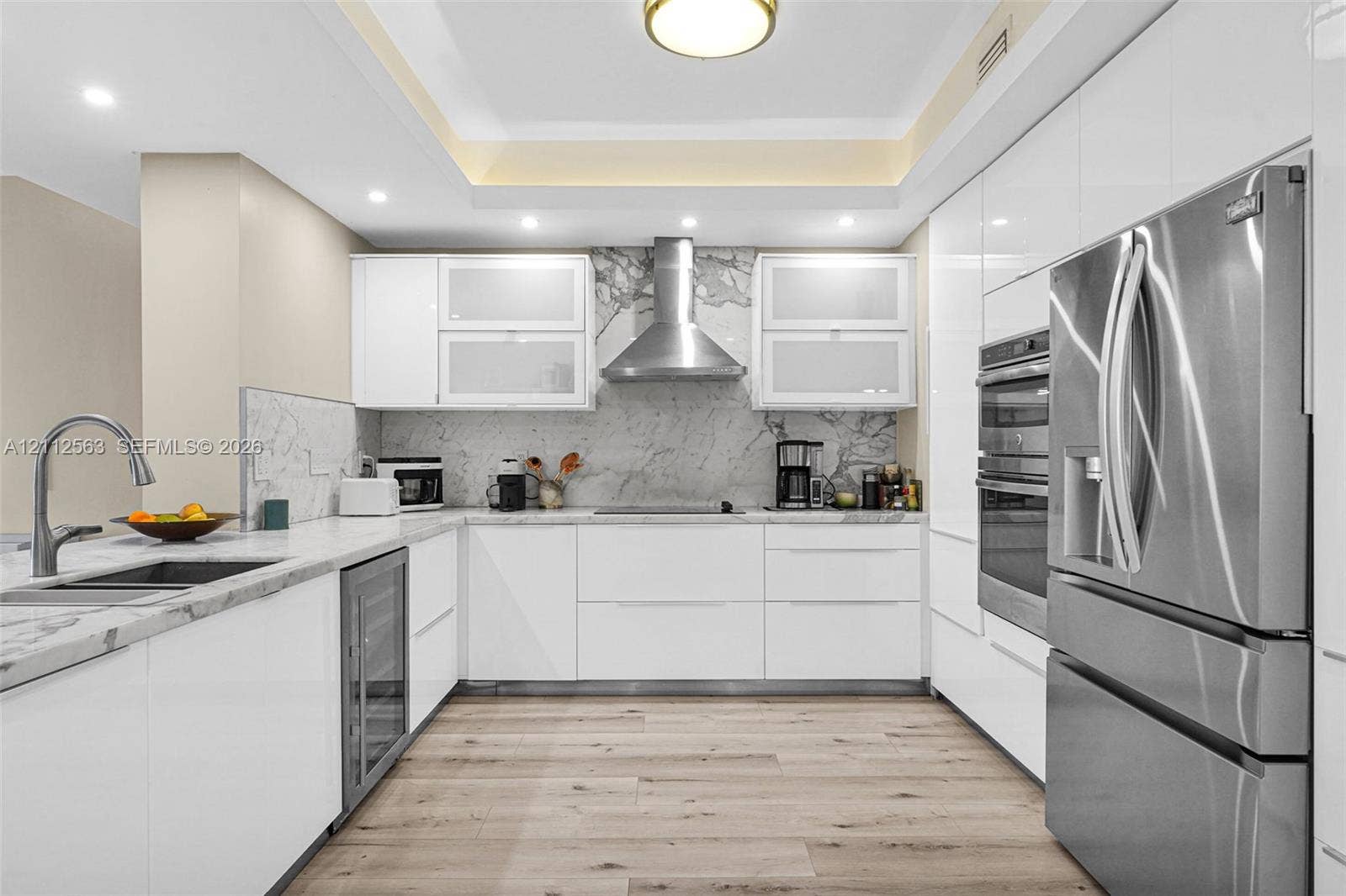 3330 NE 190th Street, #2016, Aventura, FL 33180 Contemporary kitchen featuring high-gloss white cabinetry, stone slab backsplash, stainless steel appliances, built-in dual ovens, and wood-finish flooring