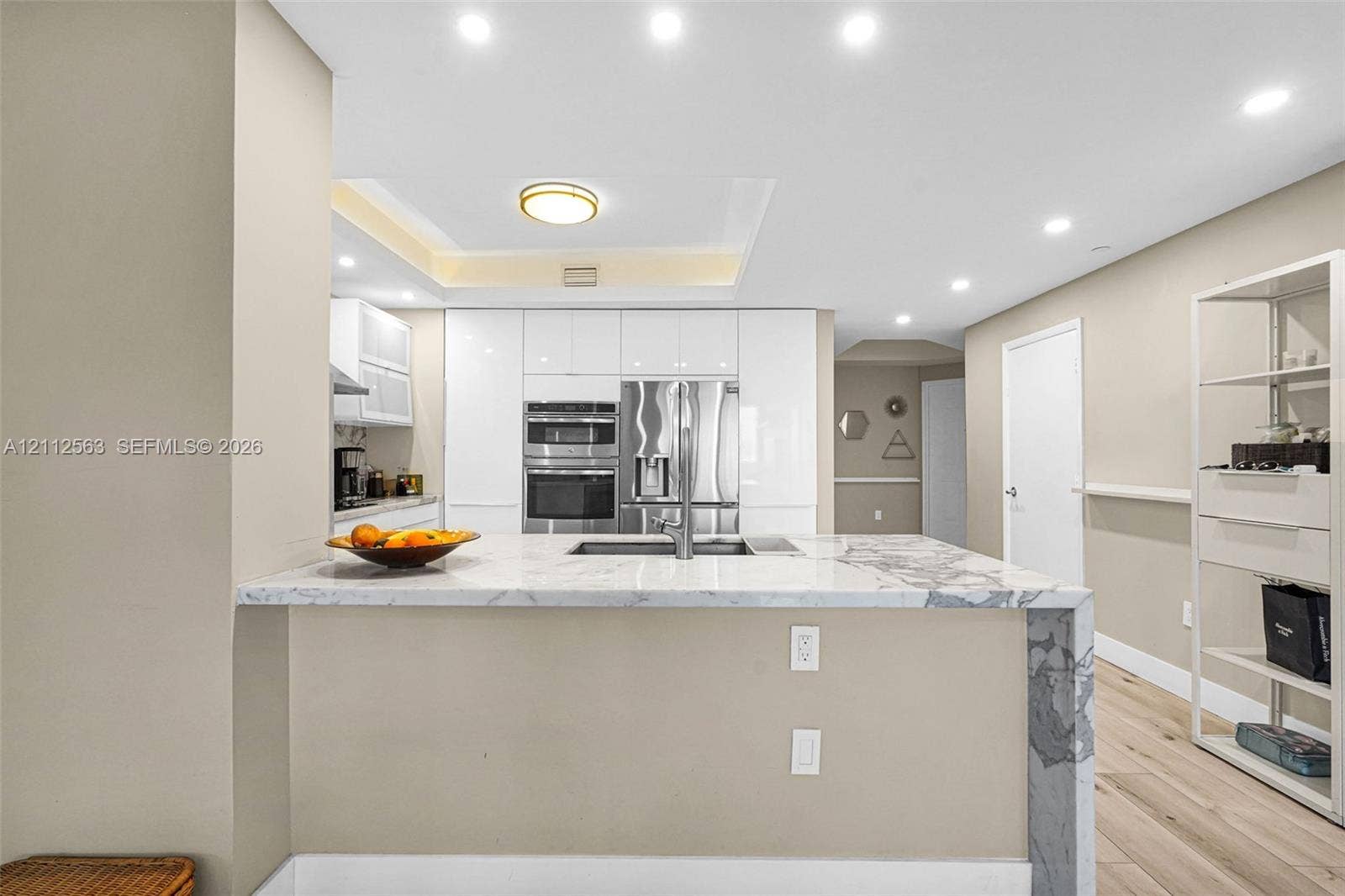 3330 NE 190th Street, #2016, Aventura, FL 33180 Kitchen featuring white slab-front cabinetry, a waterfall-edge stone island, integrated stainless steel appliances, recessed lighting, and wood-finish flooring