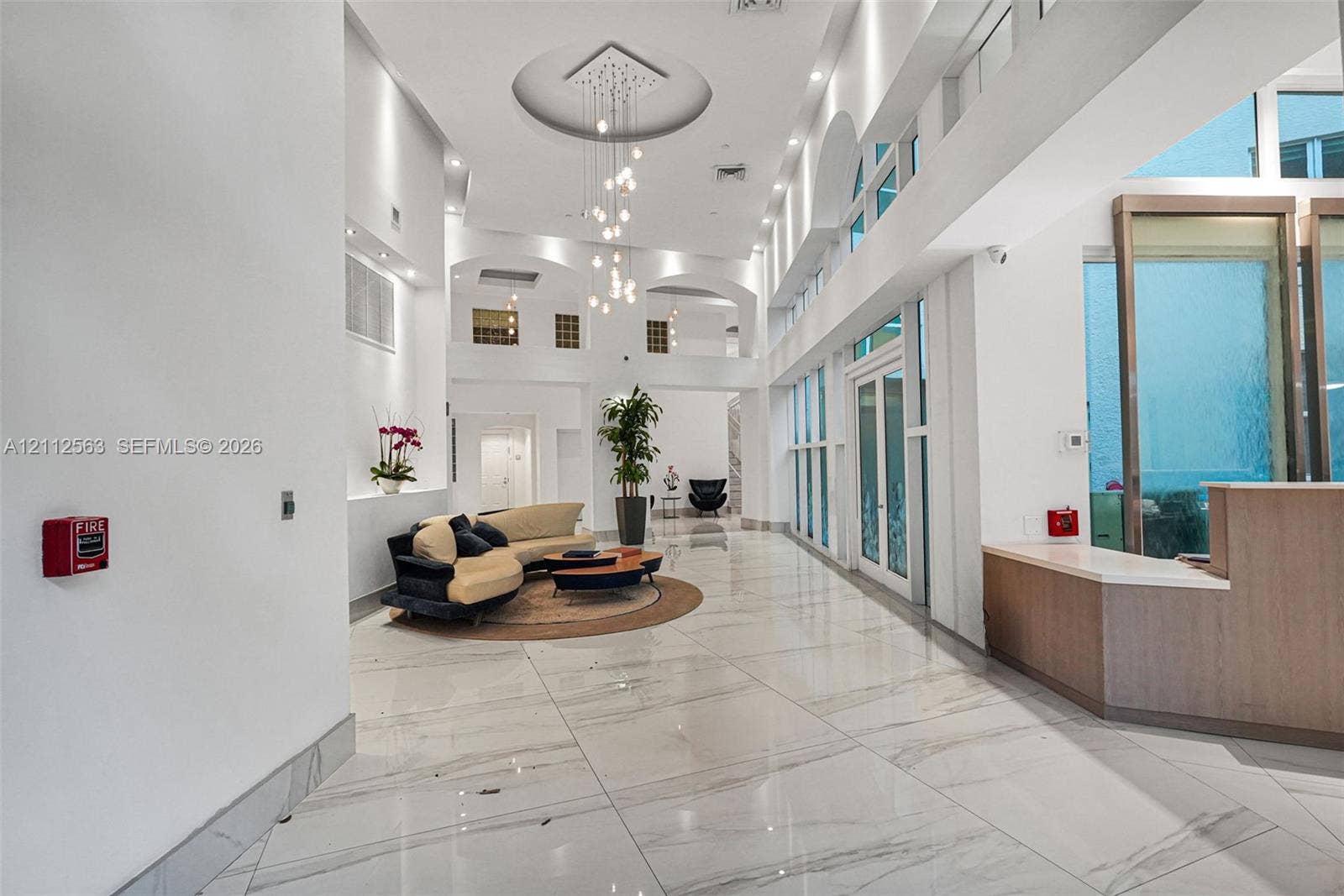 3330 NE 190th Street, #2016, Aventura, FL 33180 Grand foyer featuring double-height ceilings, stone-finish flooring, floor-to-ceiling windows, arched architectural details, and a tiered modern chandelier