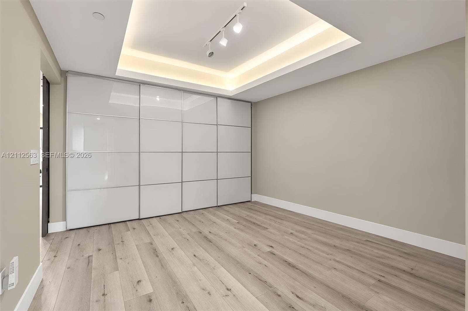3330 NE 190th Street, #2016, Aventura, FL 33180 Room featuring wood-finish flooring, built-in floor-to-ceiling white panel cabinetry, and a tray ceiling with recessed perimeter lighting and track lighting