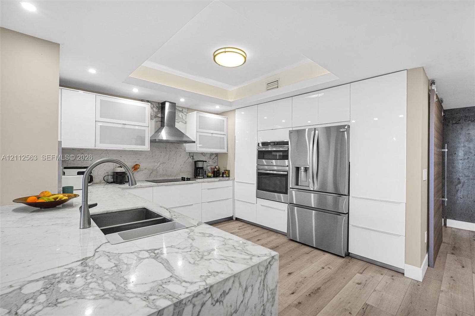3330 NE 190th Street, #2016, Aventura, FL 33180 Modern kitchen featuring floor-to-ceiling high-gloss cabinetry, stone countertops, stainless steel appliance suite, wood-finish flooring, and a recessed ceiling design