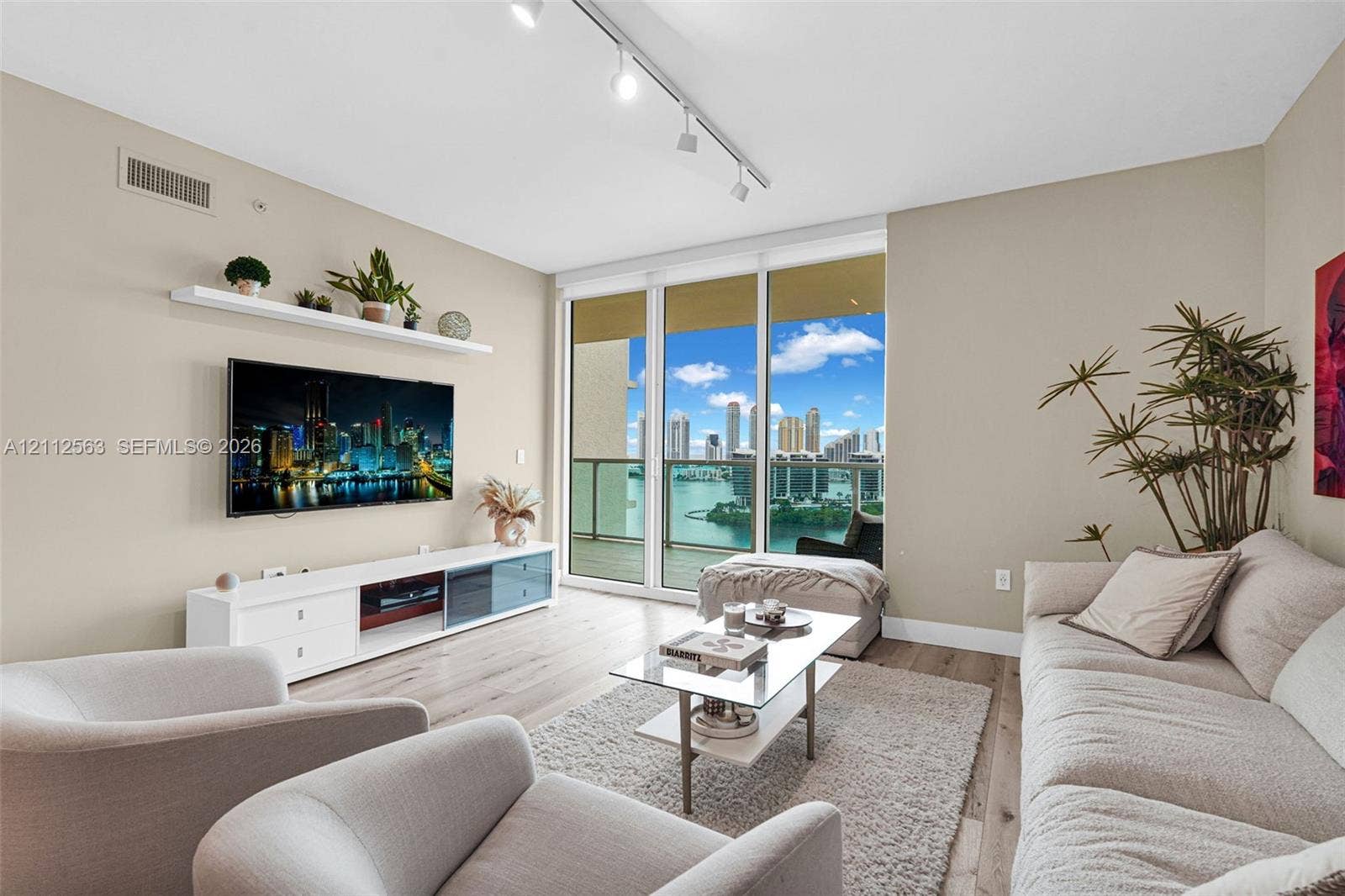 3330 NE 190th Street, #2016, Aventura, FL 33180 Living area featuring wood-finish flooring, floor-to-ceiling glass doors, built-in wall shelving, track lighting, and a private balcony