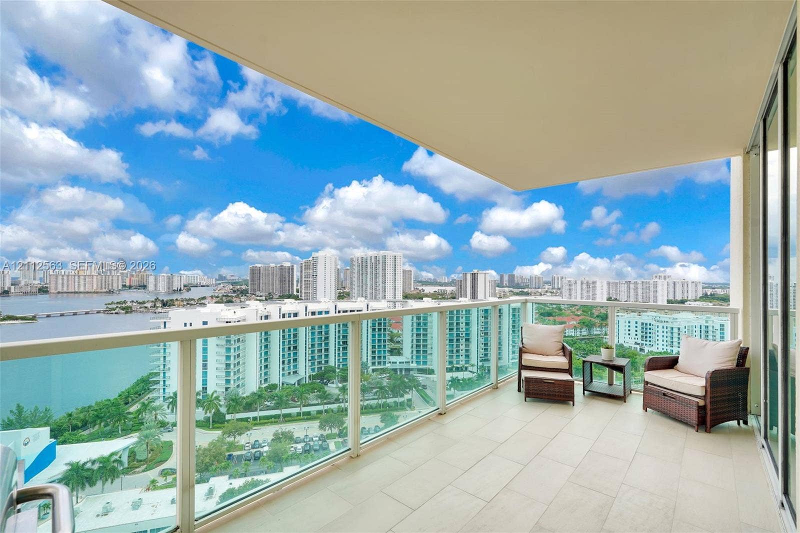 3330 NE 190th Street, #2016, Aventura, FL 33180 Covered balcony featuring neutral stone-finish flooring and a full-height glass railing, providing an unobstructed cityscape and waterfront panorama
