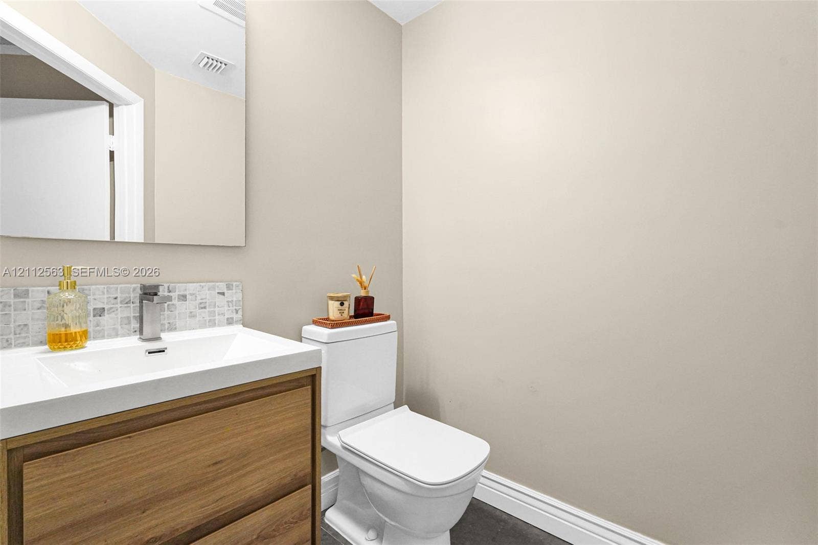 3330 NE 190th Street, #2016, Aventura, FL 33180 Vanity featuring a wood-finish cabinet with an integrated white sink, rectangular frameless mirror, and a mosaic tile backsplash