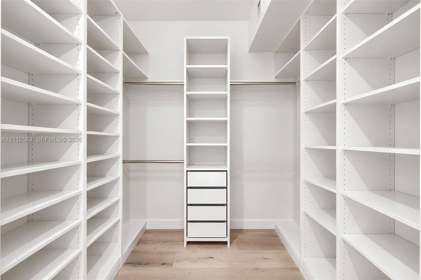 3330 NE 190th Street, #2016, Aventura, FL 33180 Walk-in closet featuring floor-to-ceiling white built-in shelving, integrated four-drawer stack, metal hanging rods, and wood-finish flooring