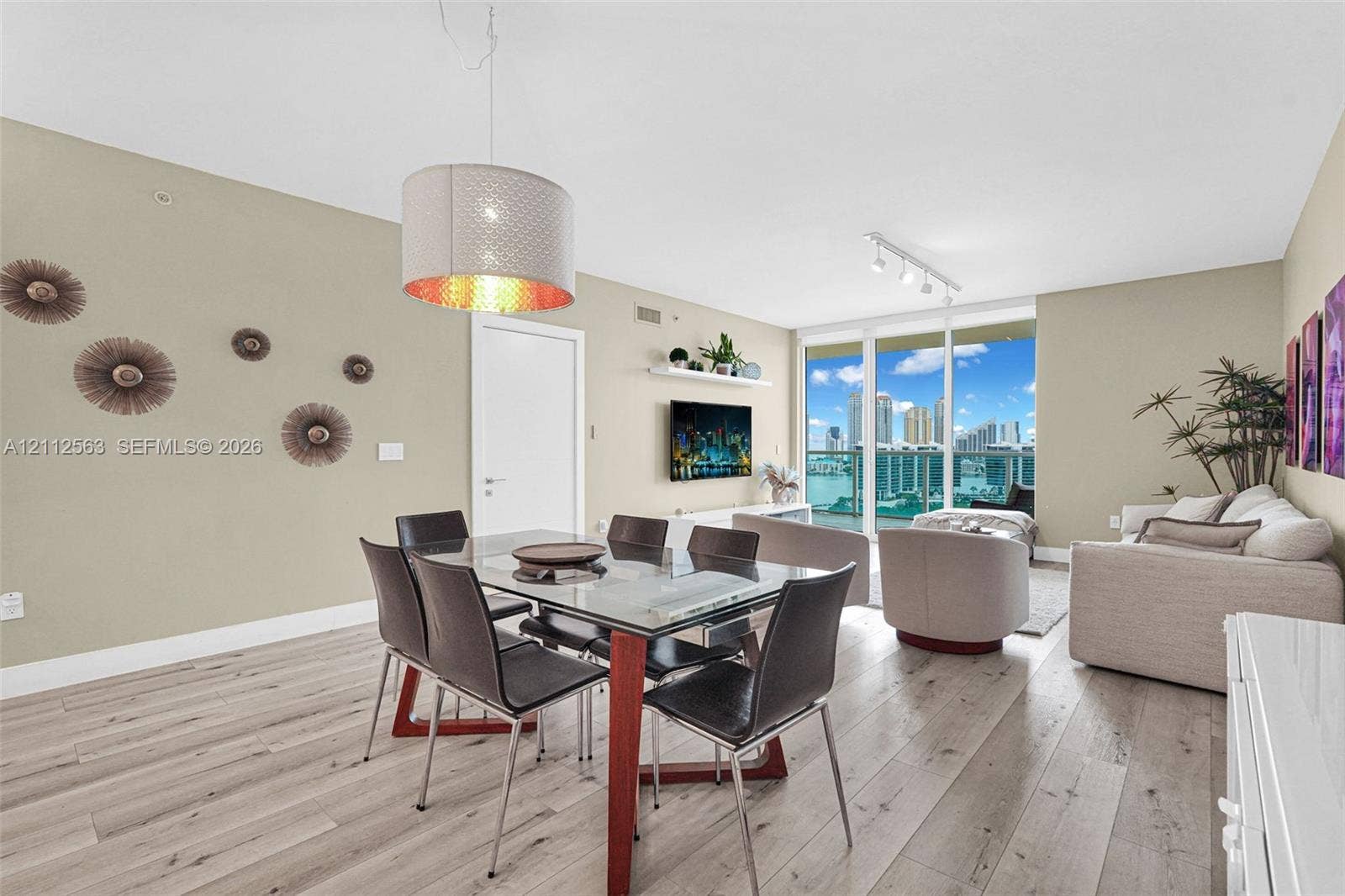 3330 NE 190th Street, #2016, Aventura, FL 33180 Open-concept living space featuring wood-finish flooring, floor-to-ceiling glass doors, cylindrical pendant lighting, a floating wall-mounted shelf, and a glass balcony railing