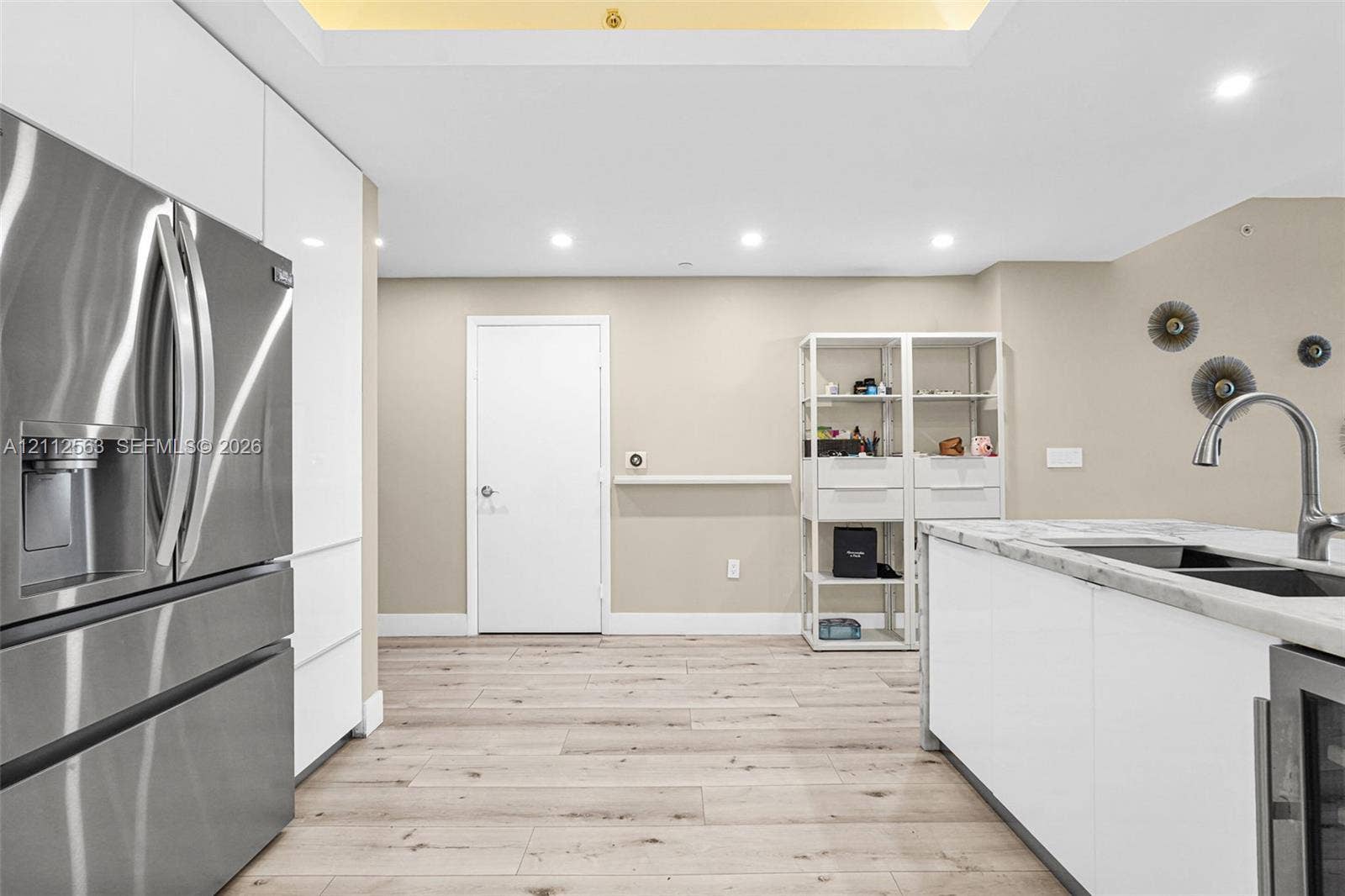 3330 NE 190th Street, #2016, Aventura, FL 33180 Kitchen featuring white flat-panel cabinetry, stainless steel refrigerator, stone-topped island with an integrated sink, wood-finish flooring, and recessed ceiling lighting