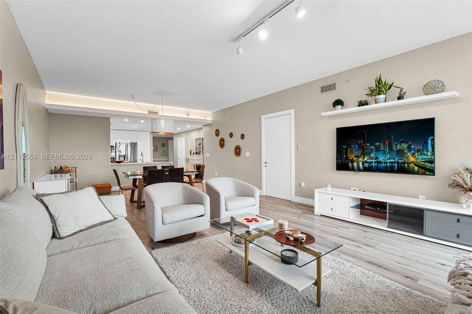 3330 NE 190th Street, #2016, Aventura, FL 33180 Open-concept living space featuring wood-finish flooring, cove lighting, adjustable track lighting, and a floating wall-mounted display shelf