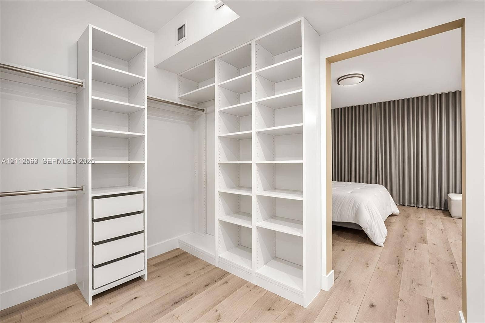 3330 NE 190th Street, #2016, Aventura, FL 33180 Custom walk-in closet featuring white built-in shelving, integrated drawers, metal hanging rods, and wood-finish flooring