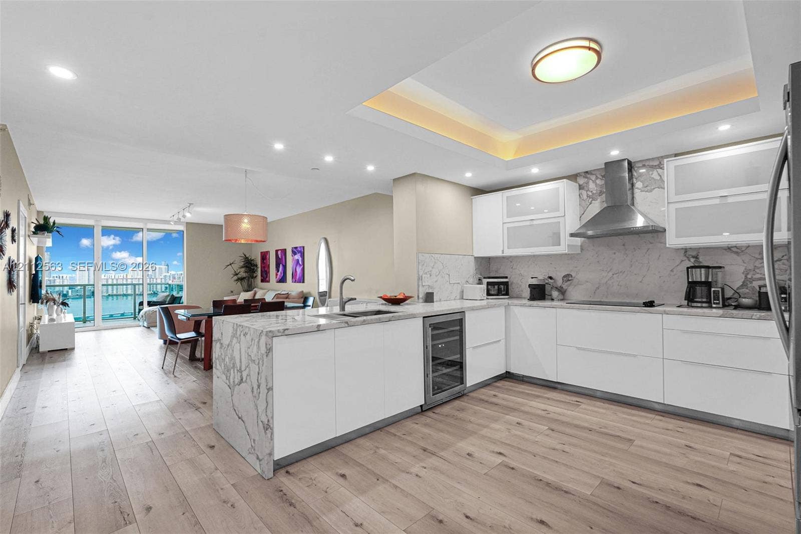 3330 NE 190th Street, #2016, Aventura, FL 33180 Kitchen featuring a waterfall-edge island, stone-finish countertops and backsplash, custom white cabinetry, built-in wine refrigeration, and recessed tray ceiling lighting