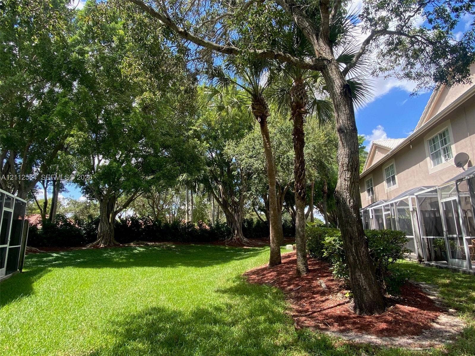 1809 Salerno Circle, Weston, Weston, FL 33327 Expansive backyard featuring a sprawling lawn, mature trees, tiered landscaping, and a screened-in rear patio enclosure
