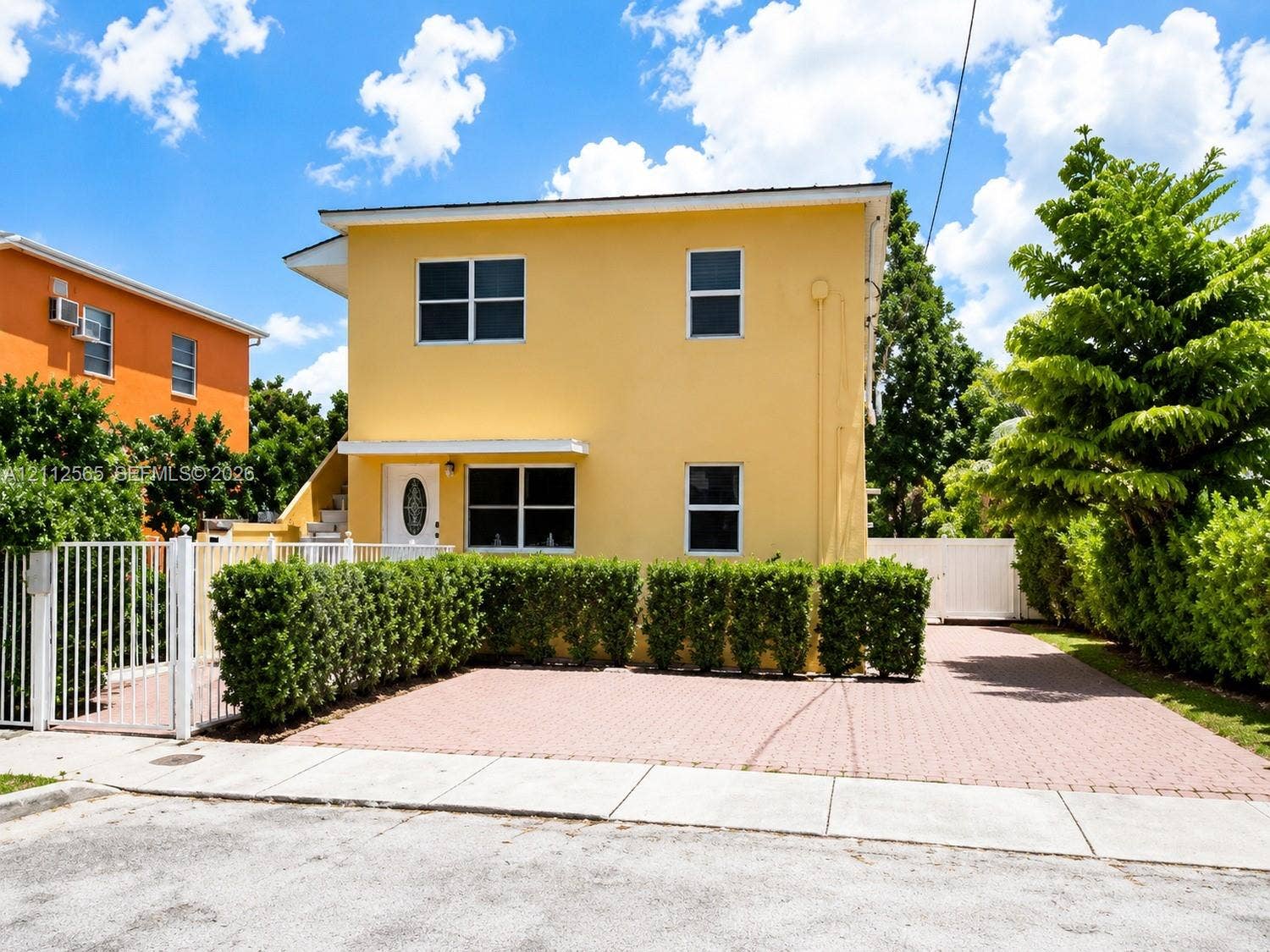 Two-story exterior featuring smooth stucco siding, a paved driveway, a gated entrance, and manicured perimeter hedges