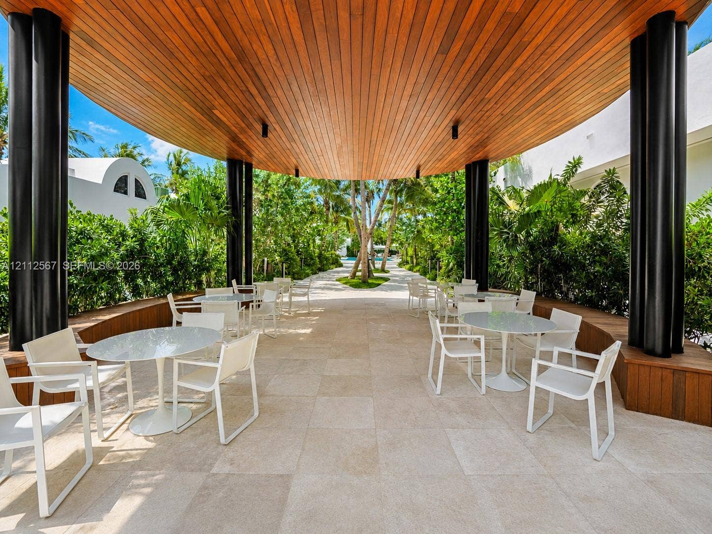 6365 Collins Avenue, #3208, Miami Beach, Miami Beach, FL 33141 Covered outdoor patio featuring a vaulted wood-slat ceiling, structural cylindrical pillars, built-in wooden bench seating, and natural stone tile flooring