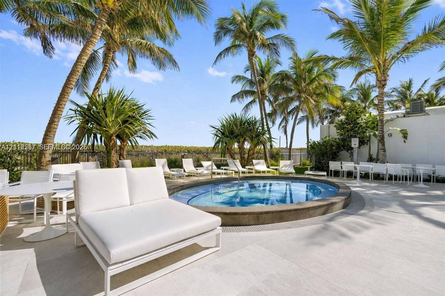 6365 Collins Avenue, #3208, Miami Beach, Miami Beach, FL 33141 Circular in-ground spa featuring a stone-finish coping, surrounded by a paved deck, mature palm trees, and perimeter fencing