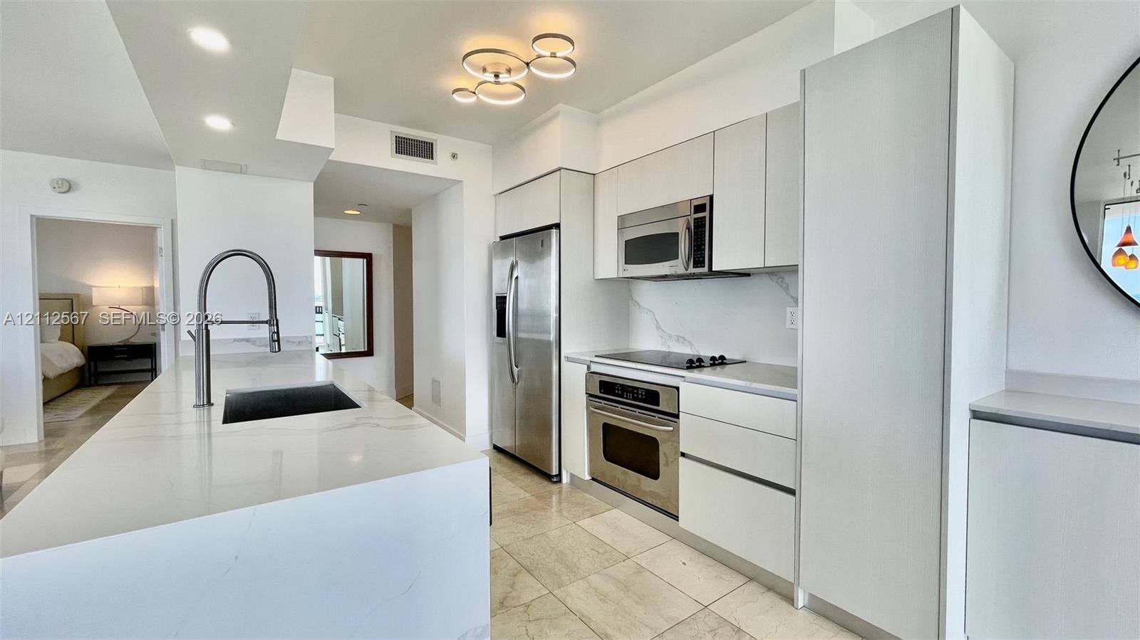 6365 Collins Avenue, #3208, Miami Beach, Miami Beach, FL 33141 Kitchen featuring white flat-panel cabinetry, light-toned stone countertops, a waterfall-edge island, stainless steel appliances, and polished stone flooring
