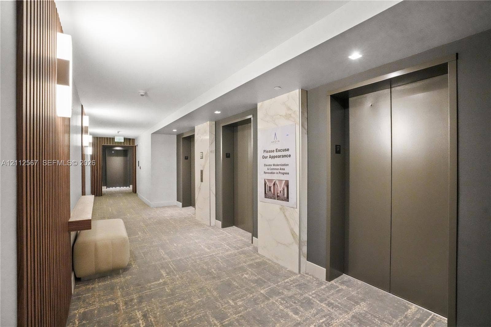 6365 Collins Avenue, #3208, Miami Beach, Miami Beach, FL 33141 Common area featuring multi-panel elevator banks, vertical wood slat wall detailing, stone-clad pillar accents, recessed ceiling lighting, and wall-mounted light fixtures