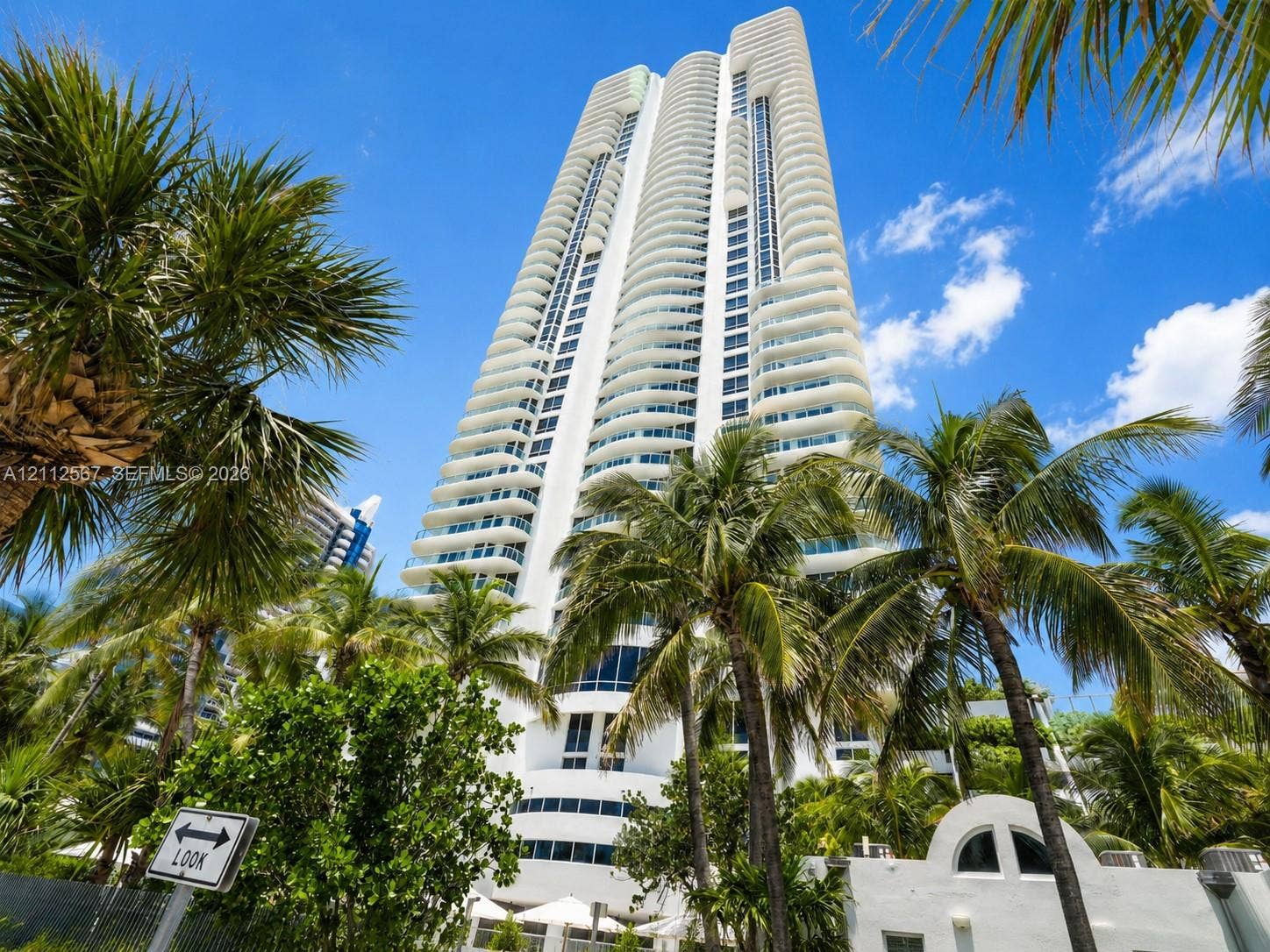 6365 Collins Avenue, #3208, Miami Beach, Miami Beach, FL 33141 High-rise building featuring curved white balconies, floor-to-ceiling glass windows, and exterior palm landscaping