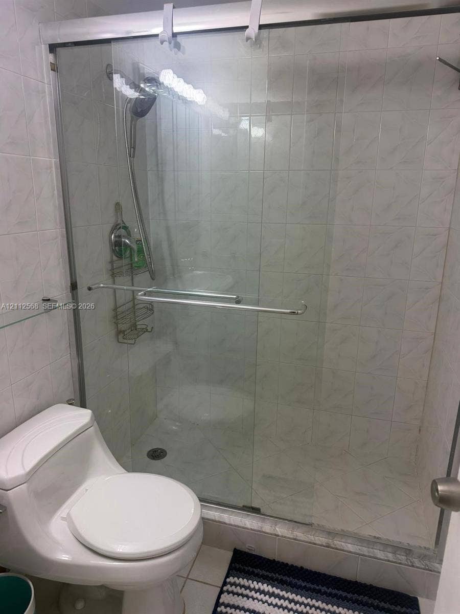 1936 S Ocean Drive, #8B, Hallandale Beach, Hallandale Beach, FL 33009 Walk-in shower enclosure with glass sliding doors, chrome hardware, adjustable handheld shower fixture, and floor-to-ceiling tile surround