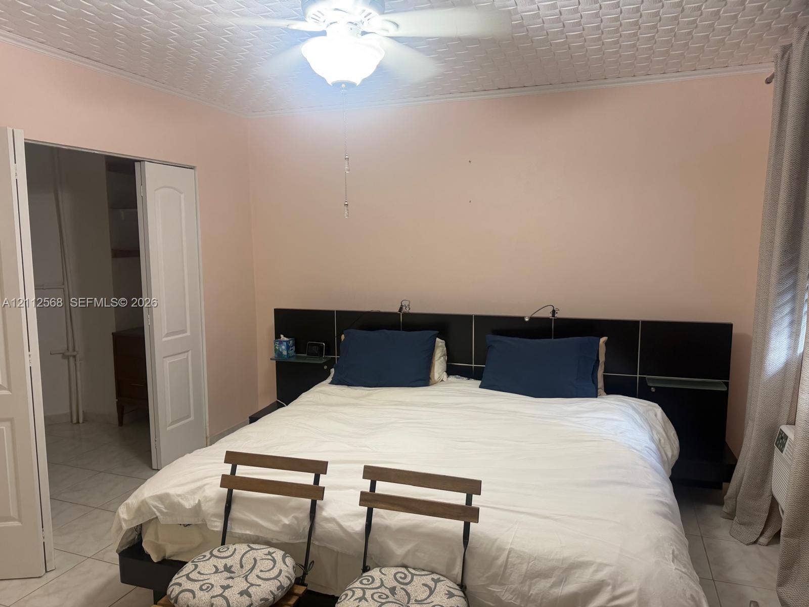 1936 S Ocean Drive, #8B, Hallandale Beach, Hallandale Beach, FL 33009 Bedroom featuring a textured tile ceiling, integrated black headboard with built-in shelving, white tile flooring, ceiling fan with light fixture, and a double-door closet