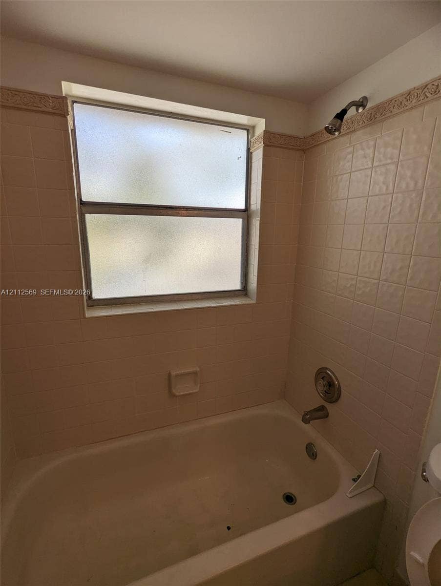 Bathtub and shower combination featuring tiled surround, built-in soap niche, frosted glass window, and chrome plumbing fixtures